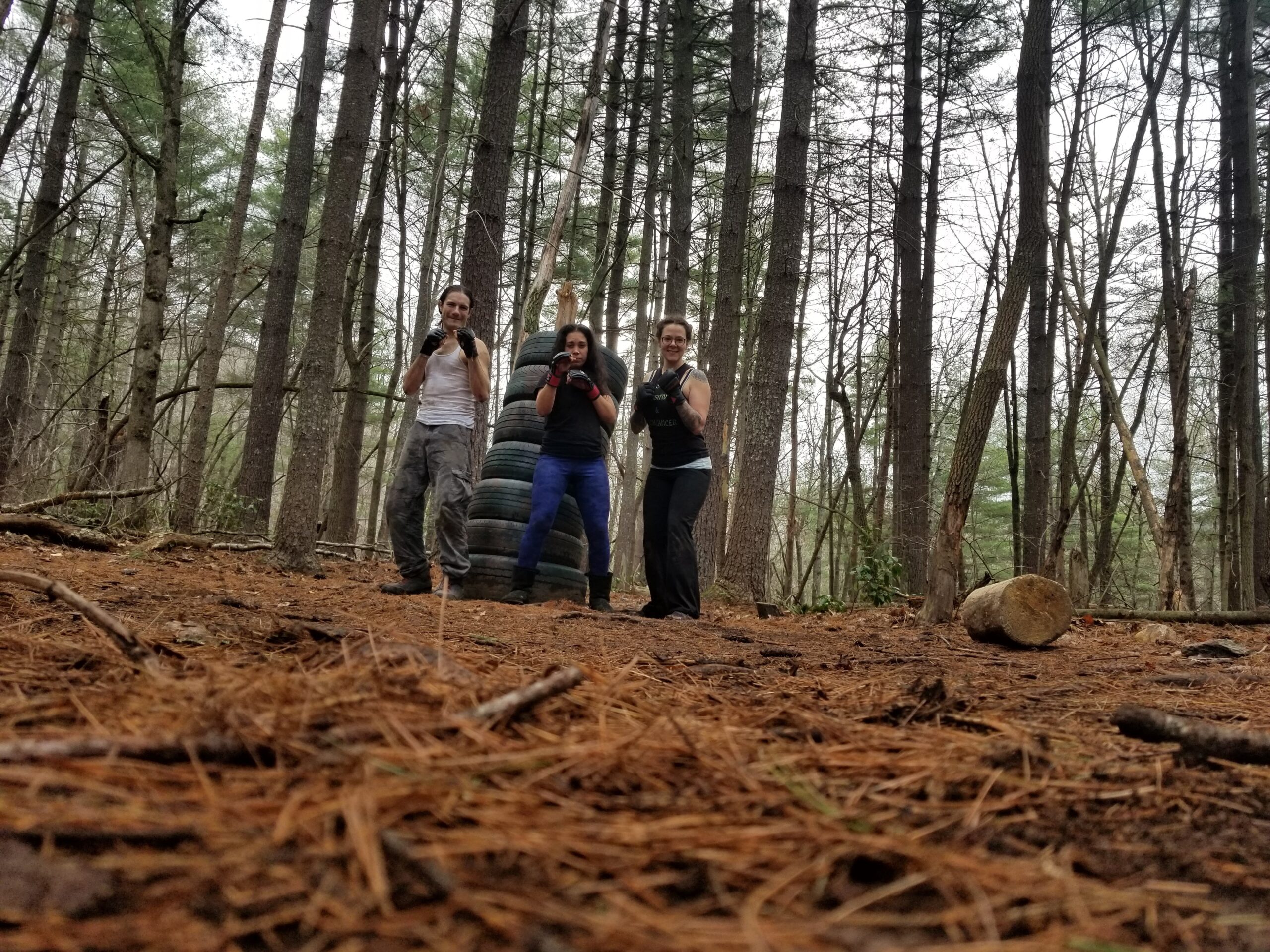 Three people training outdoors beside a stack of tires