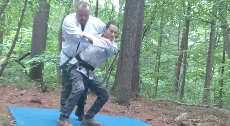 A hip throw practiced outdoors on a forest mat