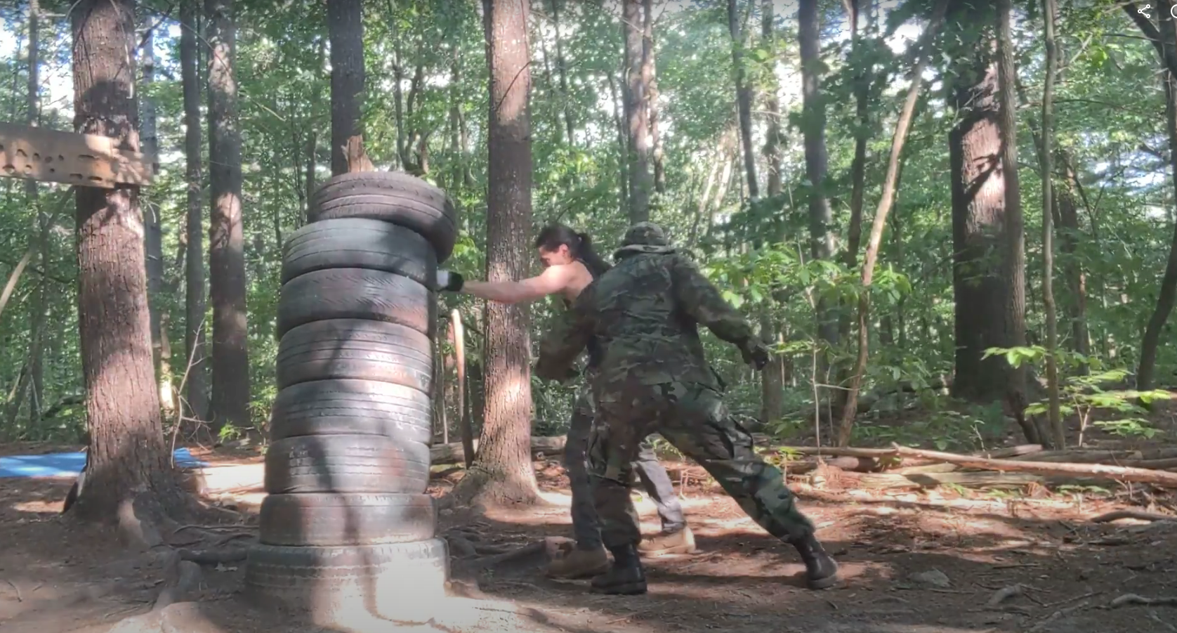 Two people striking a stack of tires in the woods